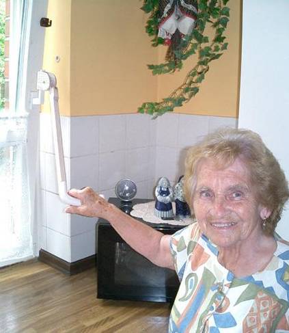 Ein ältere Frau kippt mit Hilfe der Fenstergriffverlängerung ein Fenster, dass durch eine Küchenarbeitsplatte verstellt ist.